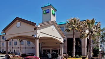 A Holiday Inn Express building with a central entrance, palm trees, and a clear blue sky.