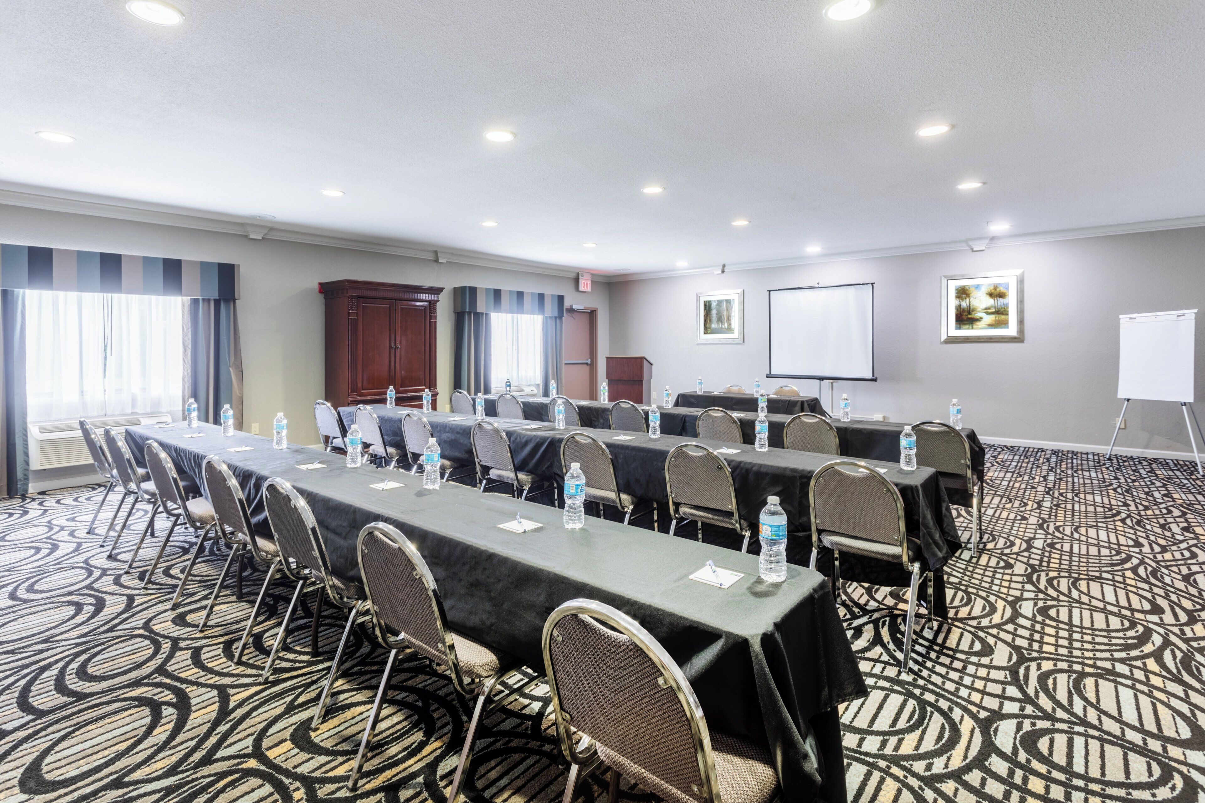 A conference room with a long table, chairs, water bottles, a projector screen, and a whiteboard.