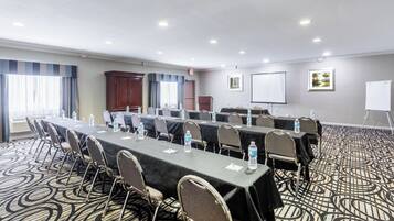 A conference room with a long table, chairs, water bottles, a projector screen, and a whiteboard.