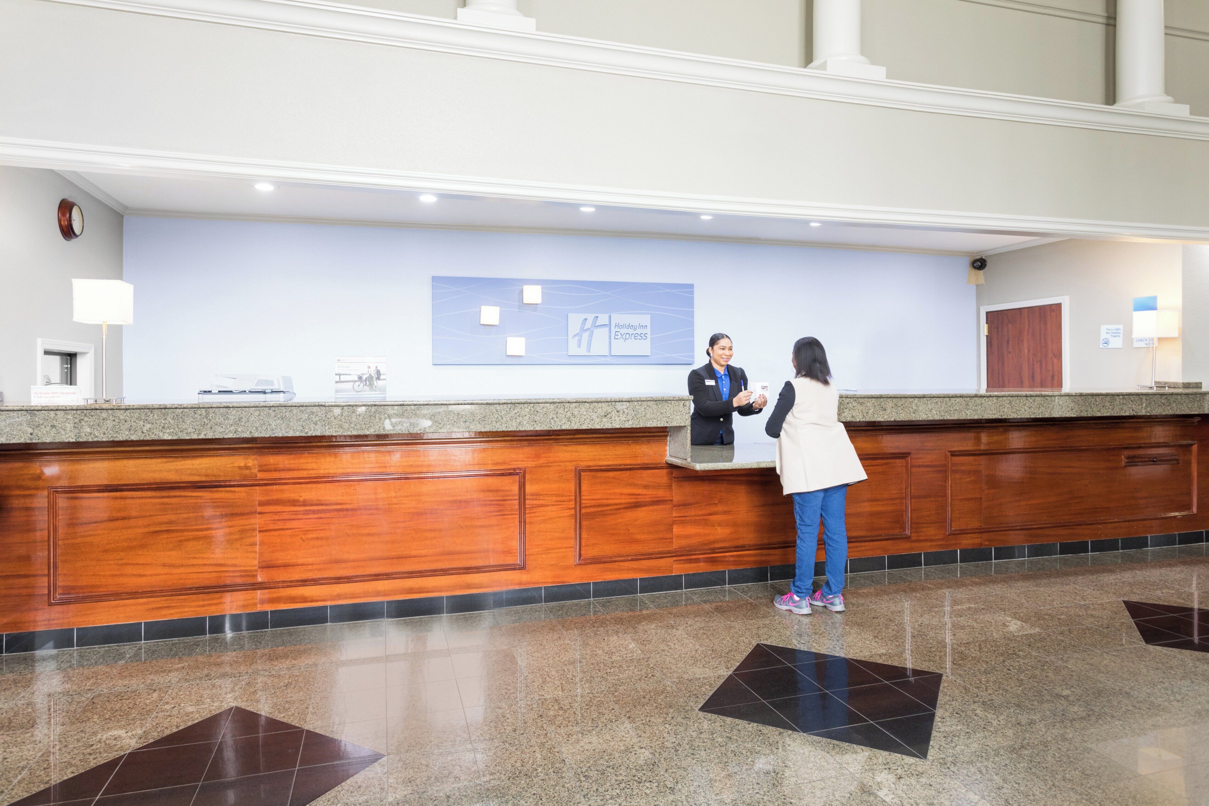 Zona de recepción de hotel con mostrador de mármol, un reloj en la pared y un cartel que indica Holiday Inn Express.
