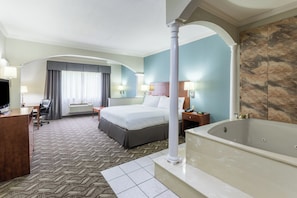 A hotel room with a large bed, a desk, a chair, a television, a bathroom with a bathtub, and a large window with curtains. - Holiday Inn Express Hotel & Suites Lake Charles by IHG (Lake Charles)