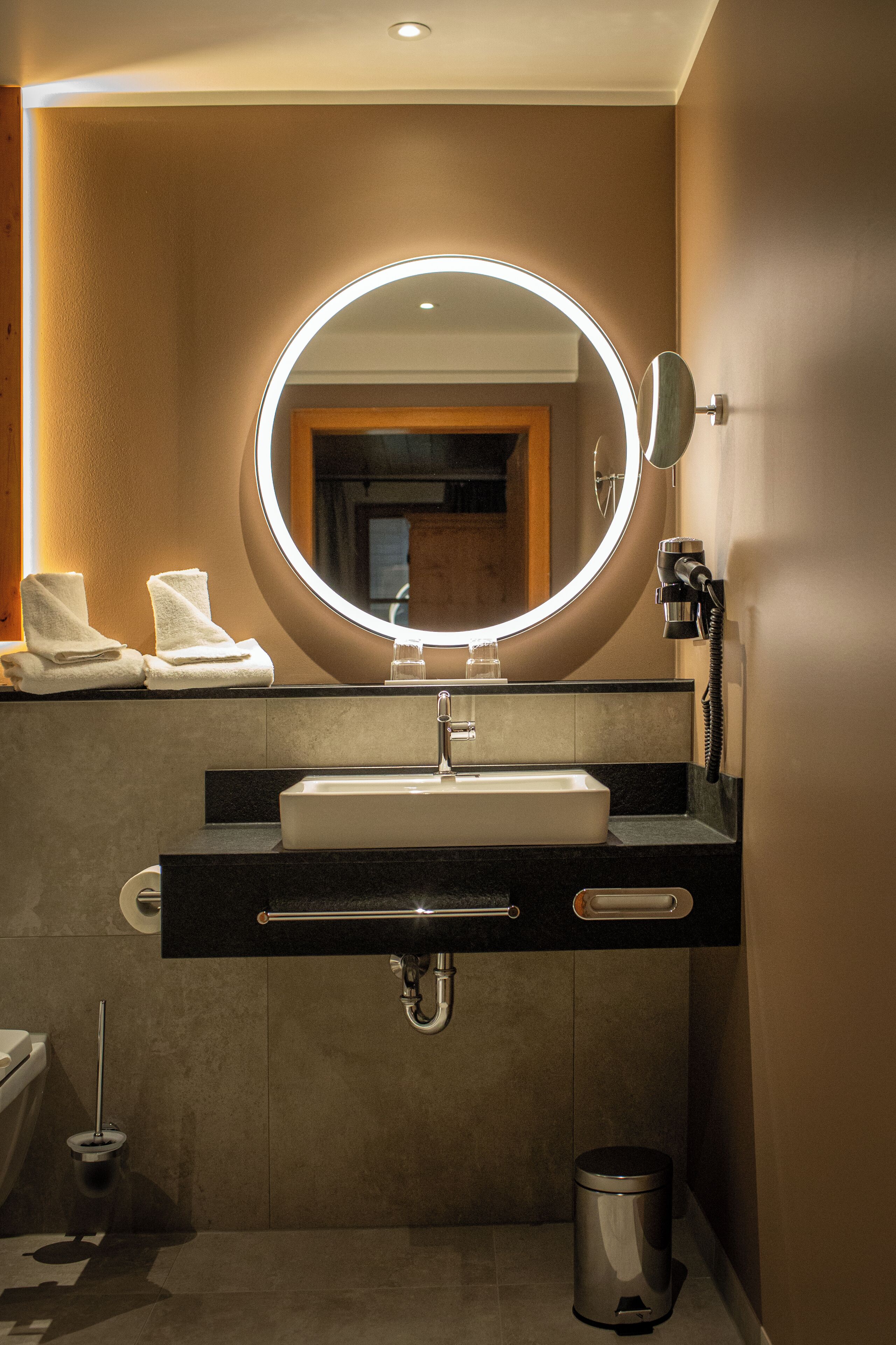 A modern bathroom with a round mirror, a sink, and a toilet.