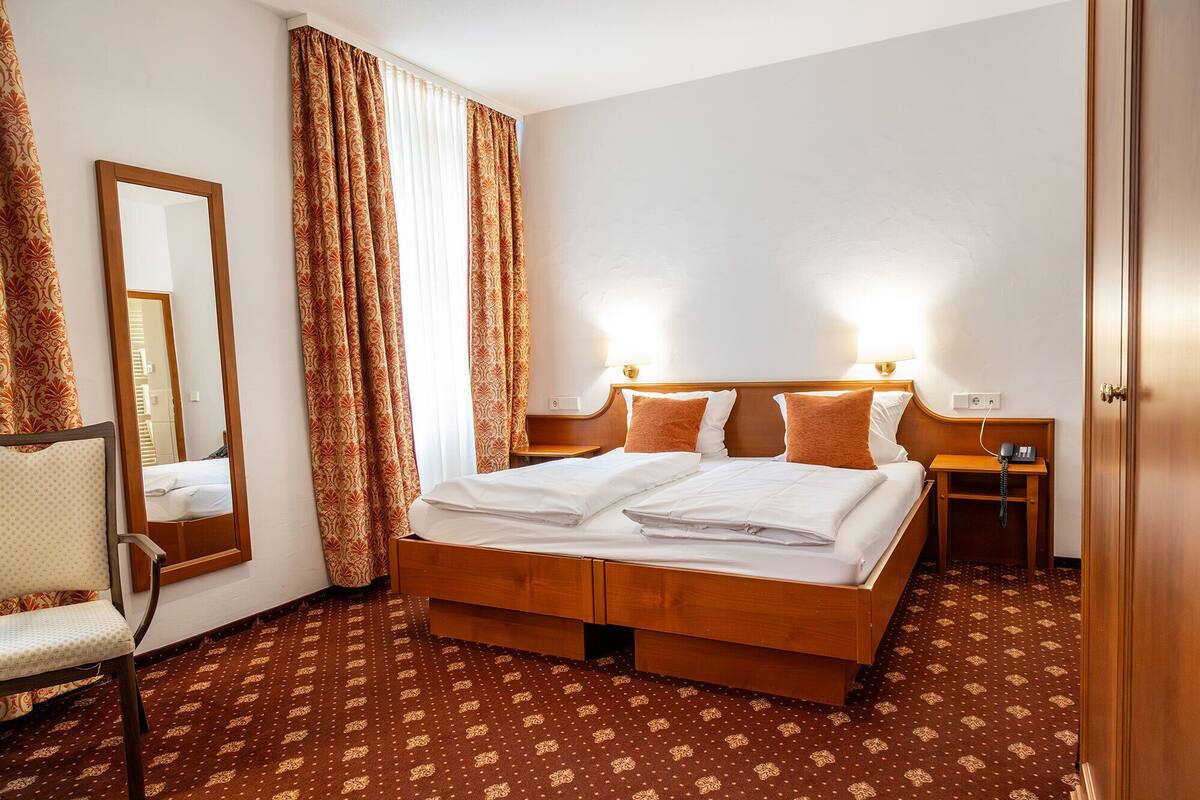 Ein Hotelzimmer mit einem großen Bett, einem Nachttisch mit Lampe, einem Sessel und einem Spiegel.