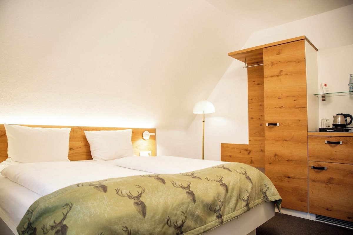 Ein Hotelzimmer mit einem Bett, einem Nachttisch, einer Lampe, einem Holzschrank und einem Wasserkocher auf dem Beistelltisch.