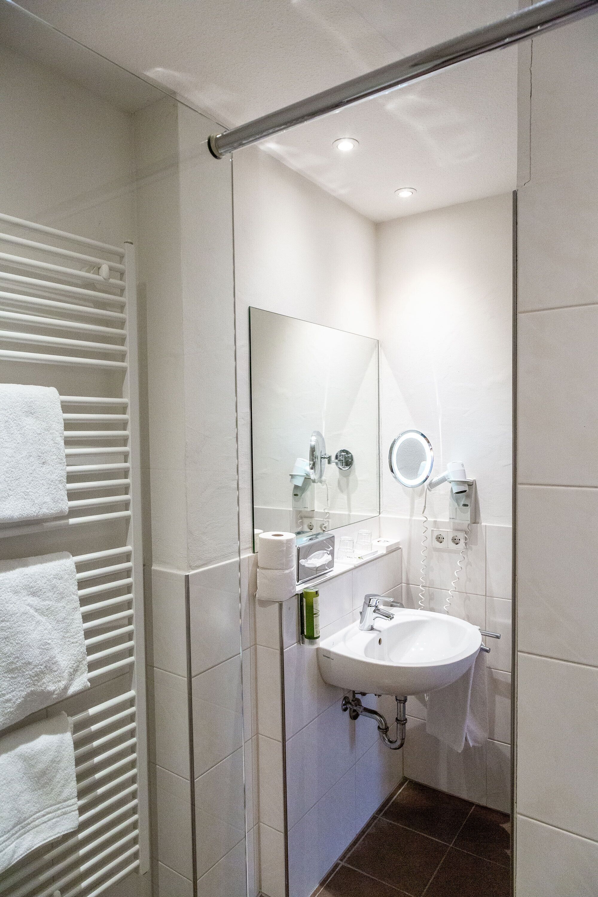 Une salle de bain moderne avec un lavabo blanc, un miroir, un porte-serviettes et un espace douche.