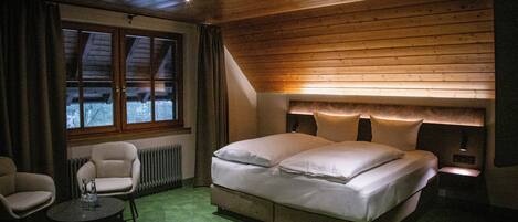 A bedroom with a large bed, a chair, a small table, and a window with curtains.