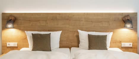 Una cama doble con ropa blanca y dos almohadas a cuadros, con lámparas de pared a cada lado.