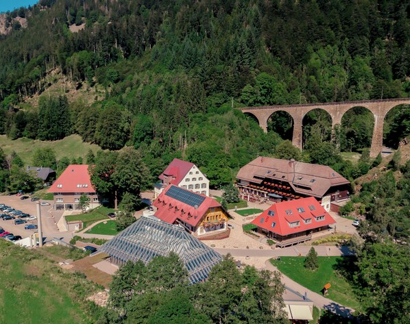 A hotel with a red roof, a glass greenhouse, and a bridge in the background. - Hotel Hofgut Sternen | Ravennaschlucht (Breitnau)