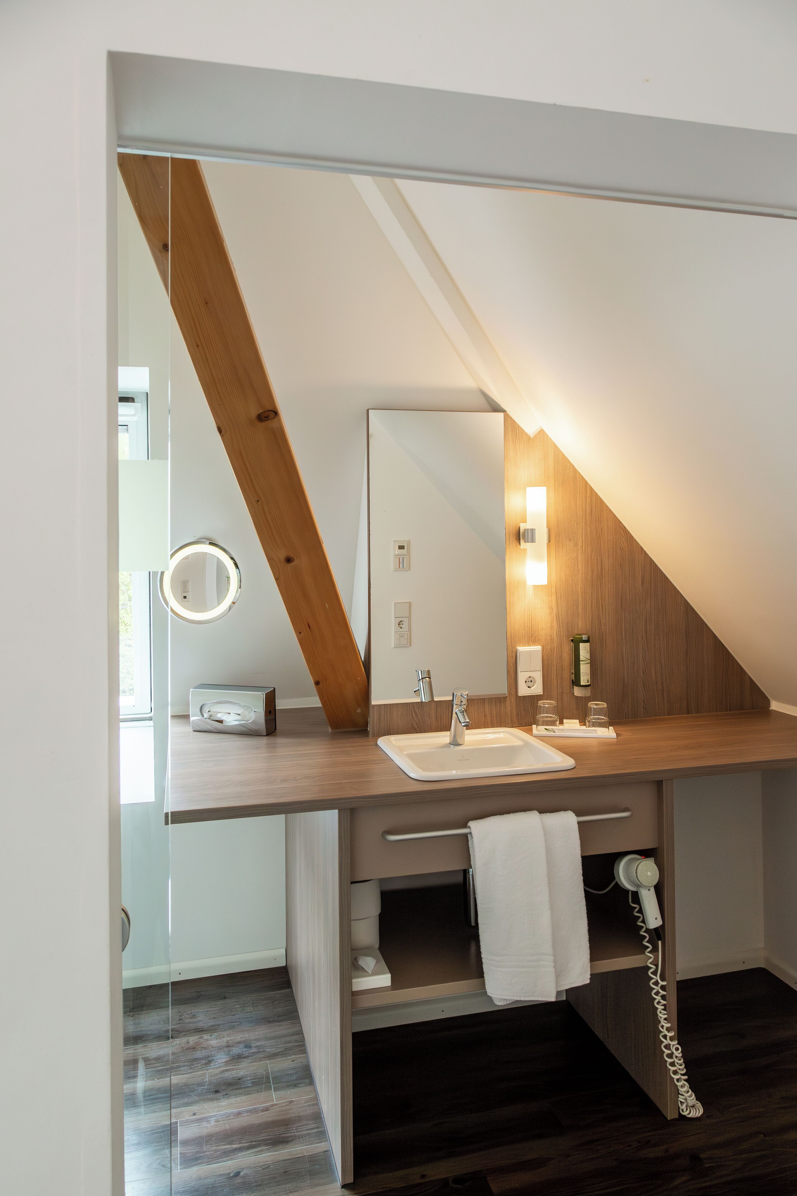 A modern bathroom with a wooden vanity, a mirror, a towel rack, and a hairdryer.
