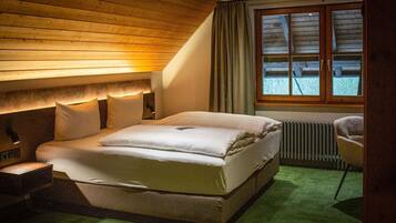 A bedroom with a wooden ceiling, a large bed with white bedding, a radiator, and a window with curtains.