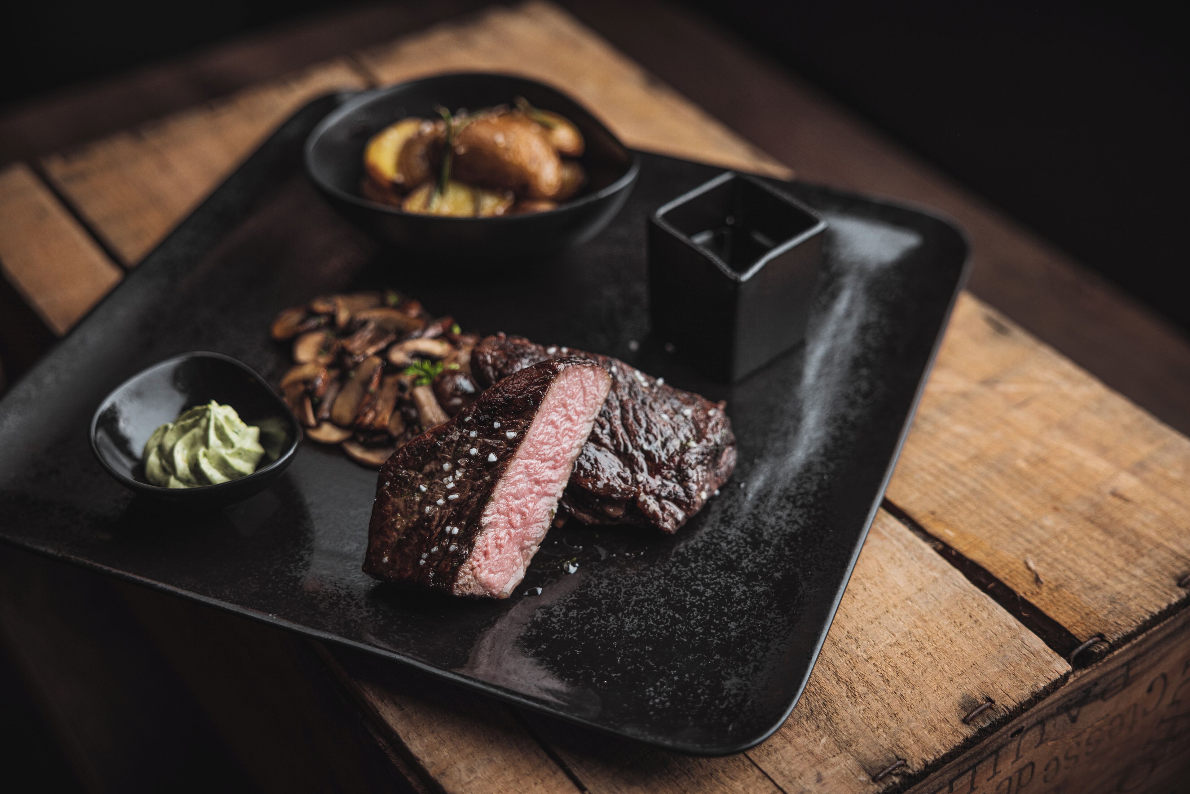 Un plato negro con un filete, champiñones y un recipiente pequeño de salsa.
