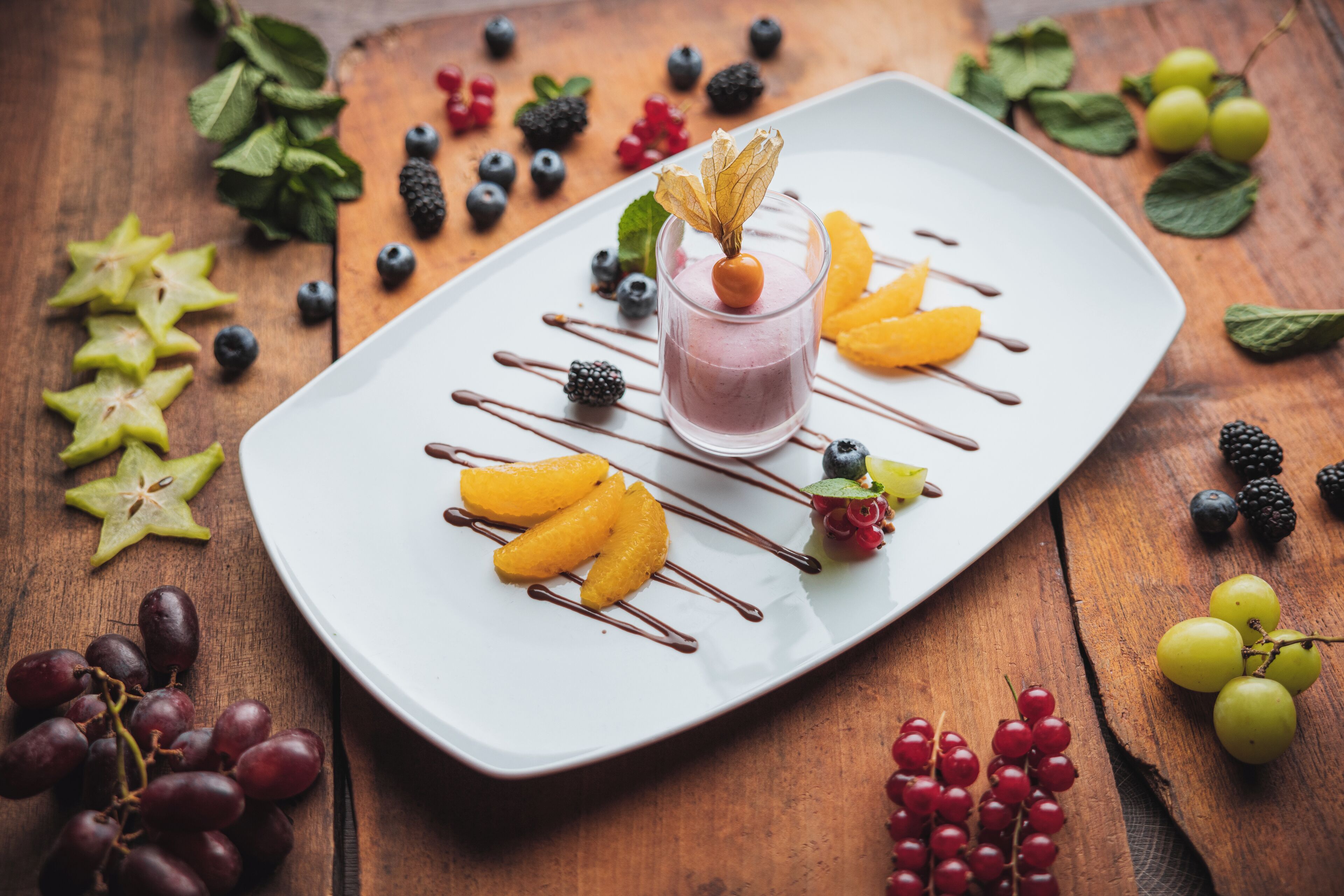 A dessert plate with a glass of pink drink, surrounded by various fruits and berries.