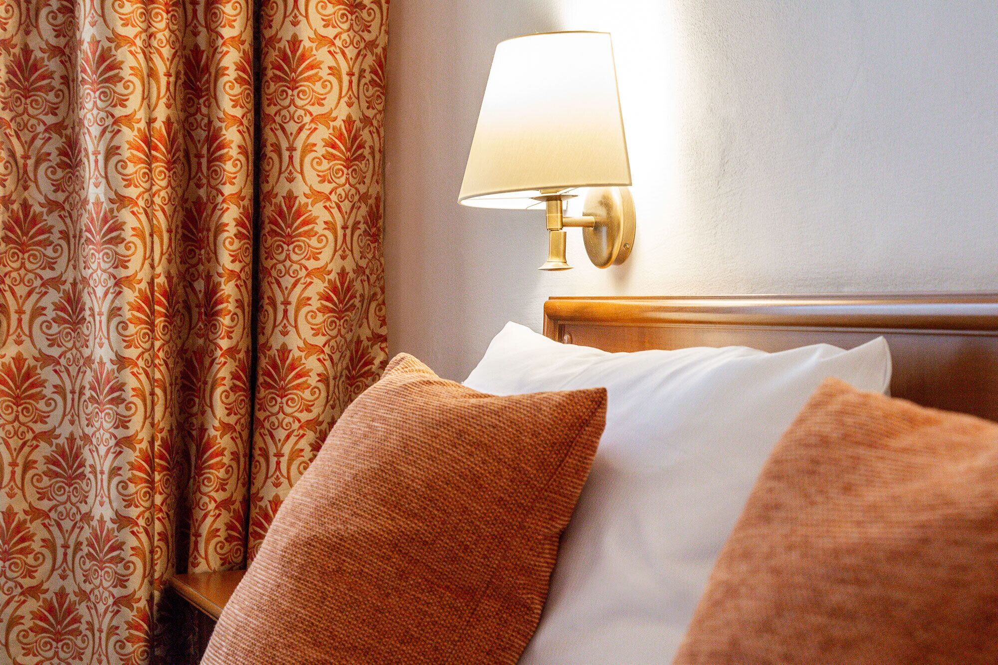 Habitació d'hotel amb un llit, cortines estampades i una làmpada penjada a la paret.