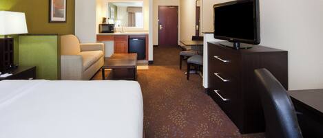 A hotel room with a bed, a desk, a television, a chair, a sofa, a small table, and a kitchenette area.