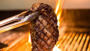 Nahaufnahme eines gegrillten Steaks, das mit einer Zange über einem Grill gehalten wird.