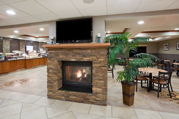 Un hall de hotel con chimenea de piedra, un televisor colocado encima, una zona de buffet y varias mesas y sillas para comer.