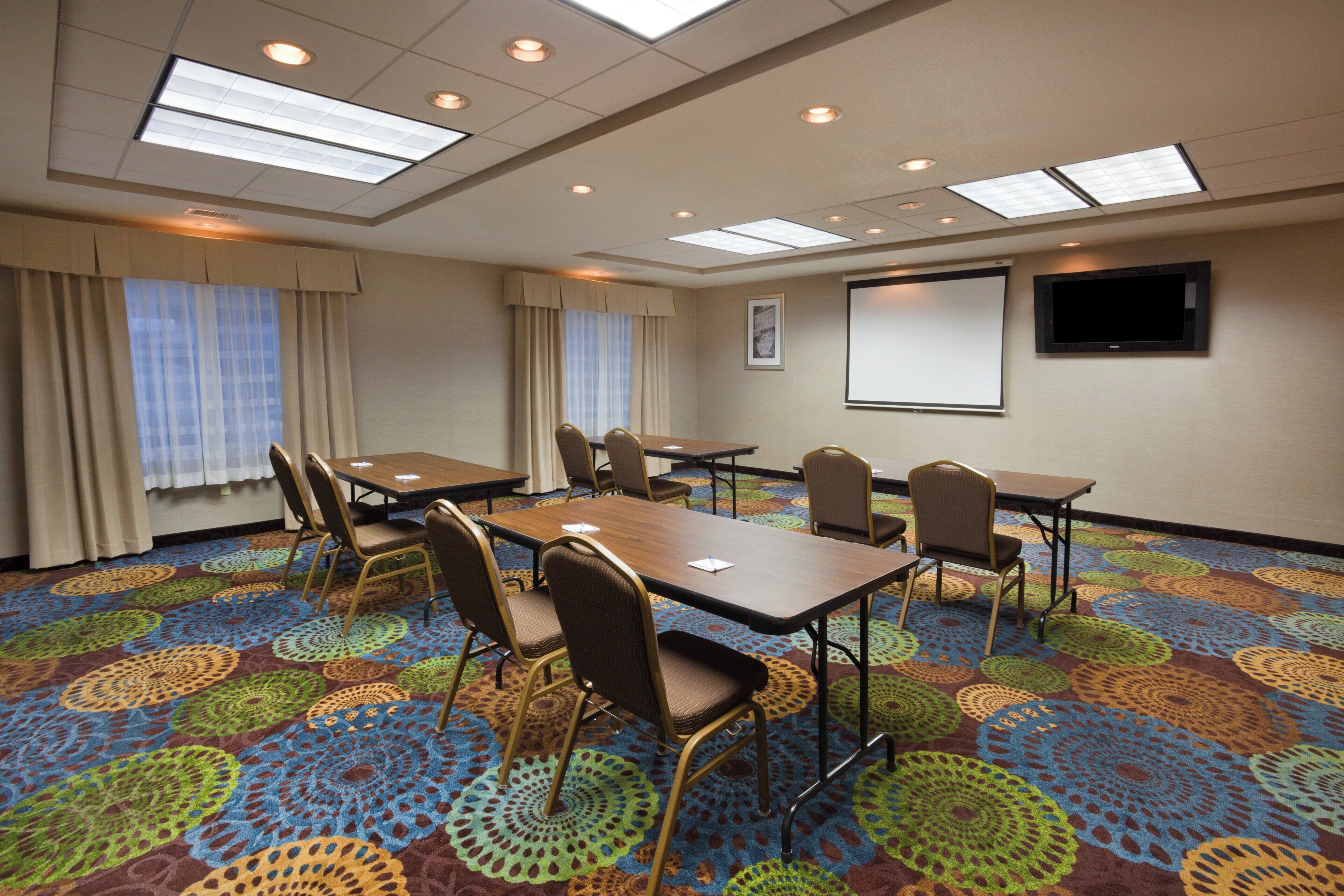 A conference room with a large table, chairs, a projector screen, and a patterned carpet.