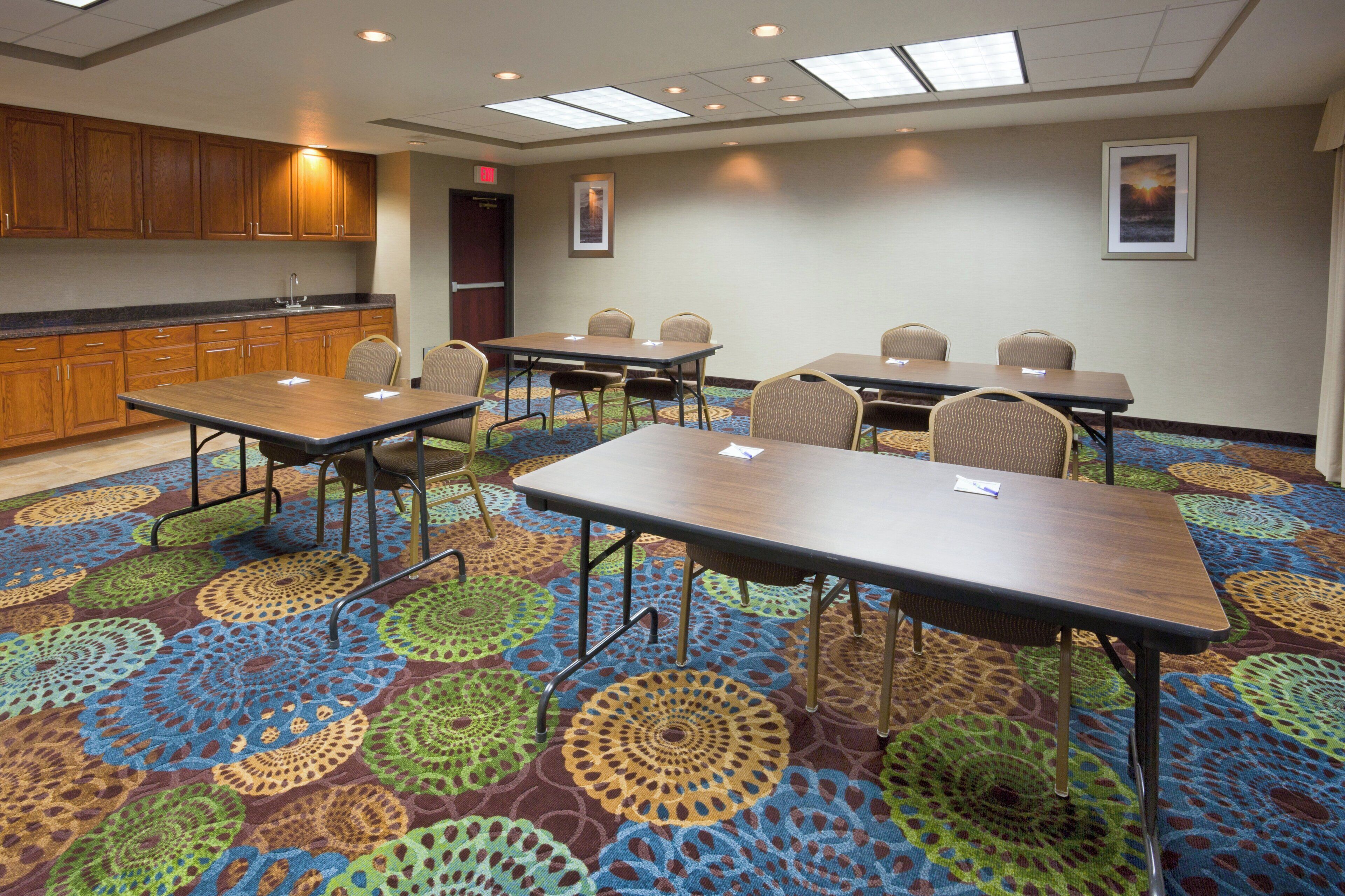 Uma sala de conferências com piso coberto por carpete, mesas de madeira e cadeiras.