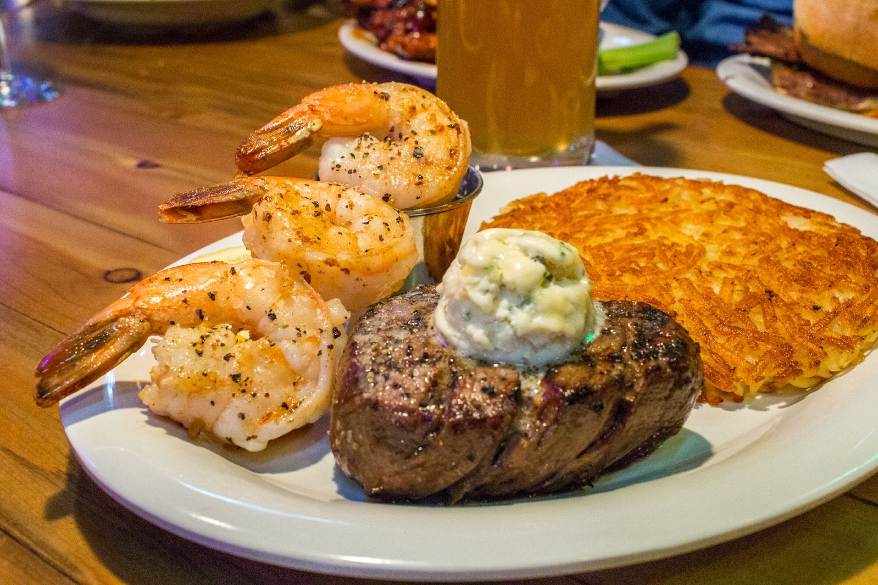 A plate with grilled steak, shrimp, and a hash brown.