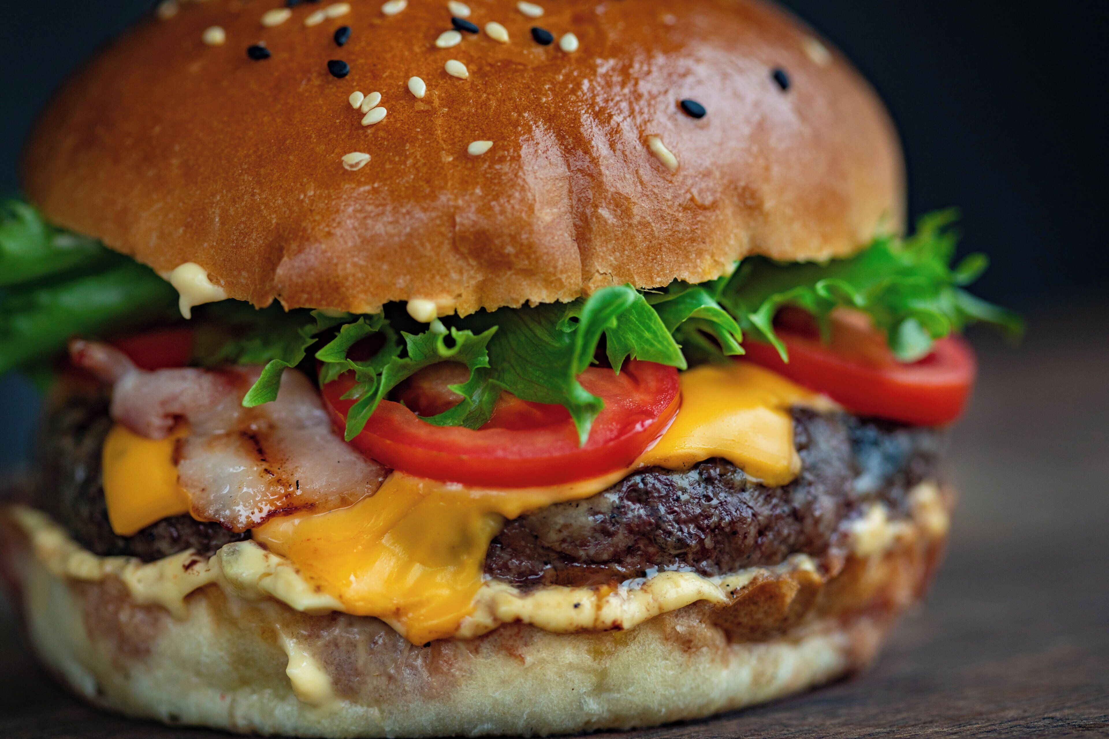 Primer plano de una hamburguesa con pan de sésamo, lechuga, tomate, queso y tocino.