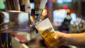 Eine Hand hält ein mit 'Mavericks' beschriftetes Glas, das von einem Zapfhahn mit Bier gefüllt wird.