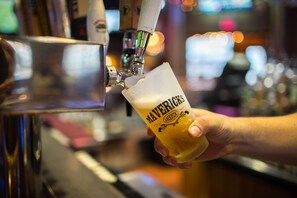 Une main tenant un verre sur lequel est écrit le mot « Mavericks », et dans lequel on verse de la bière à partir d’une tireuse.
