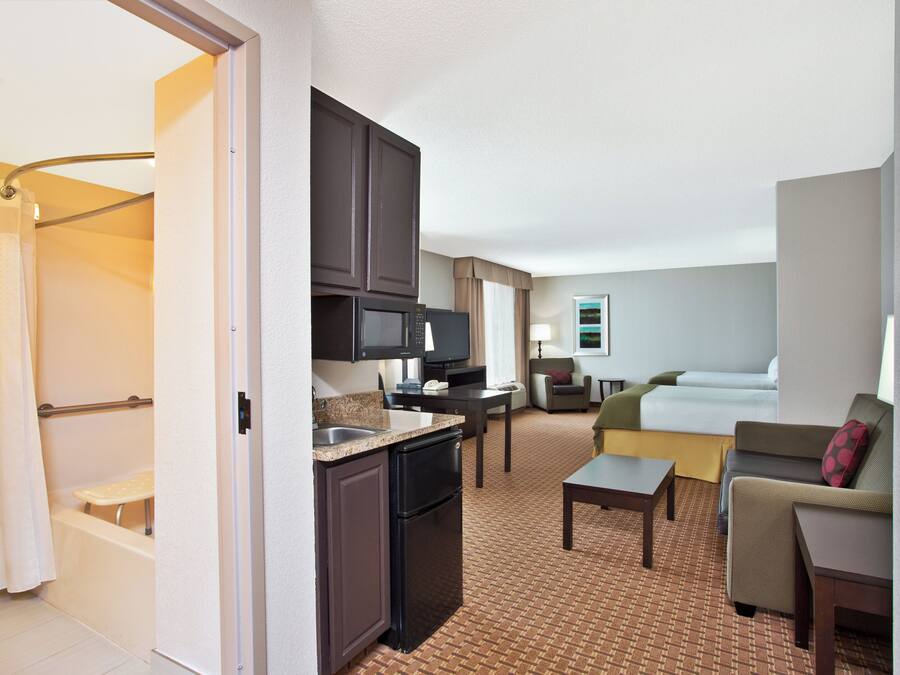 Habitación de hotel con kitchenette, baño, sala de estar con sofá y cama, y televisión.