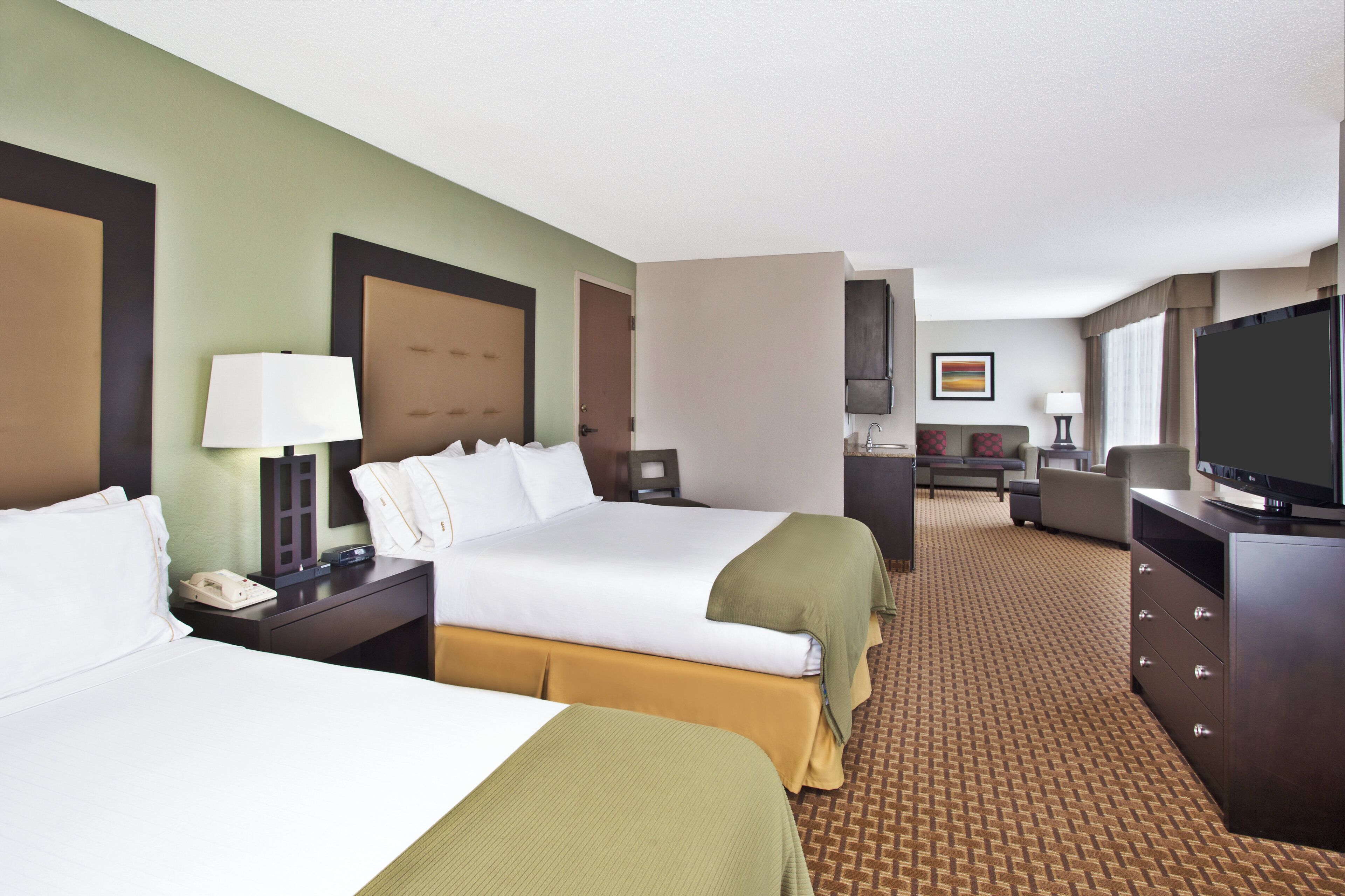 A hotel room with two beds, a desk, a television, and a seating area.