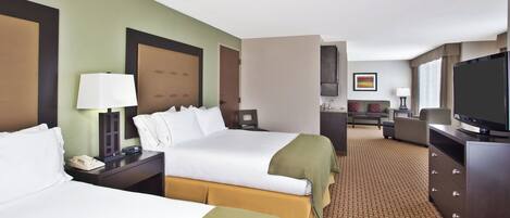 A hotel room with two beds, a desk, a television, and a seating area.
