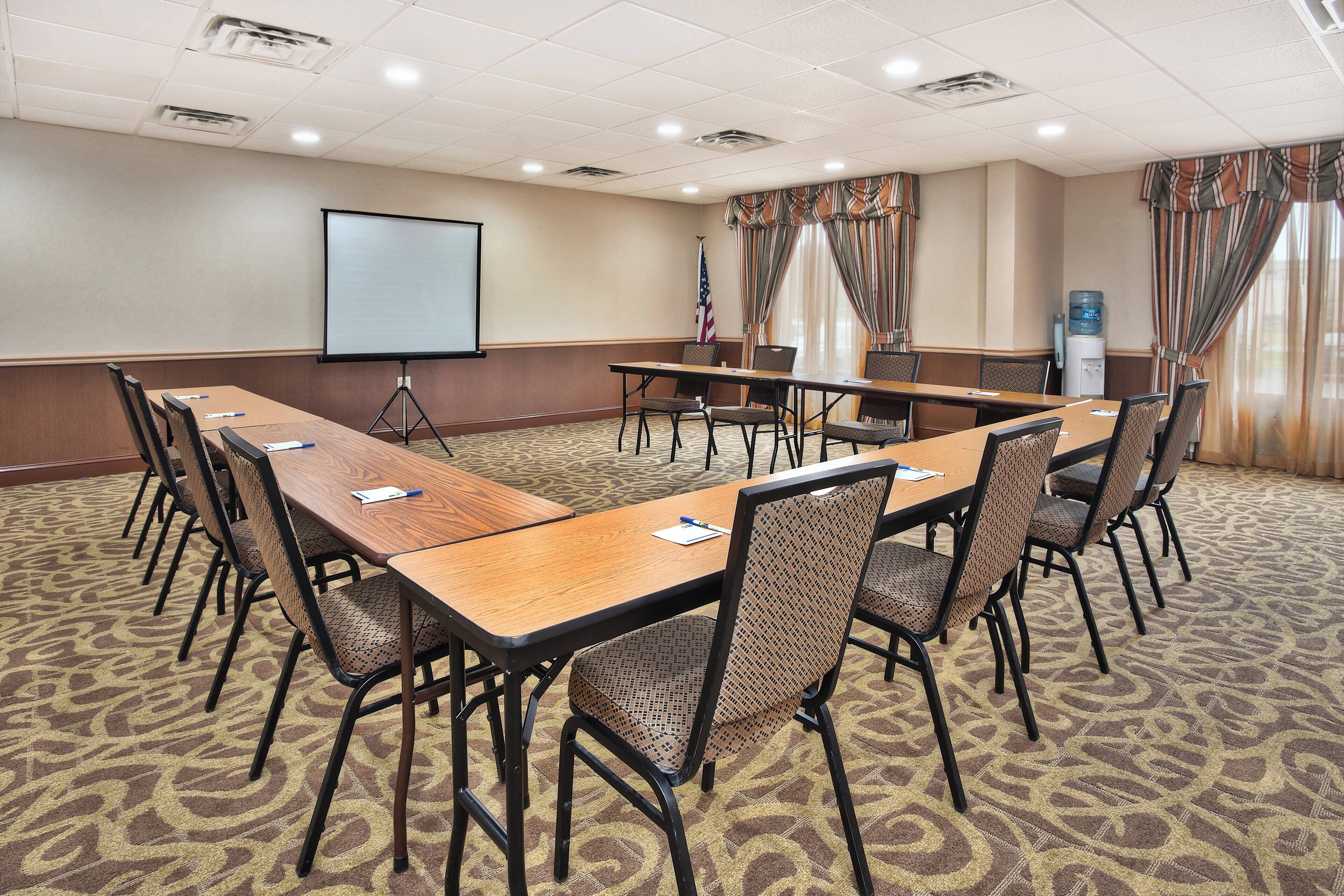 A conference room with a long table, chairs, a projector screen, and an American flag.