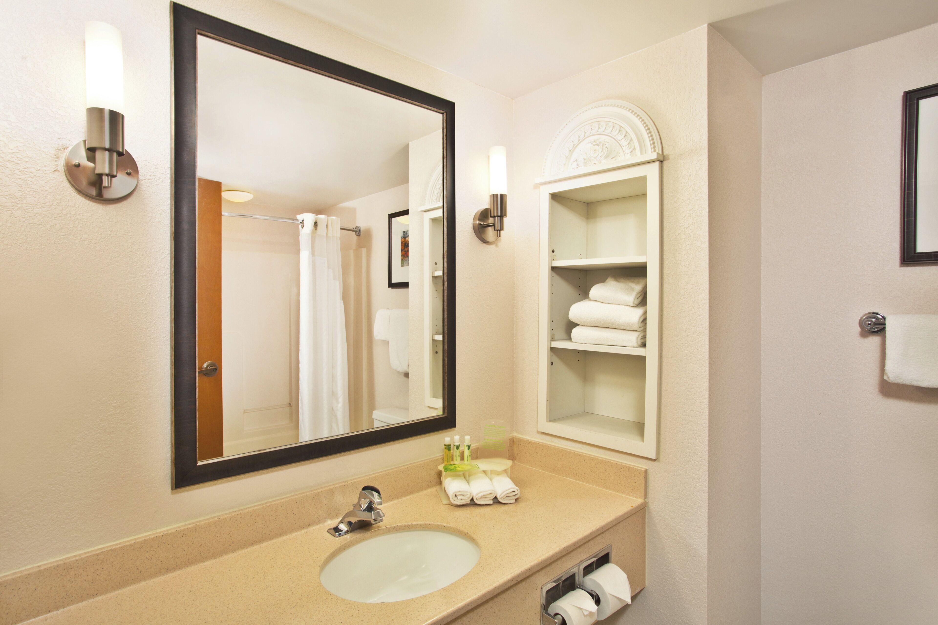 Une salle de bain avec un grand miroir, un lavabo, un porte-serviettes et une étagère avec des serviettes.