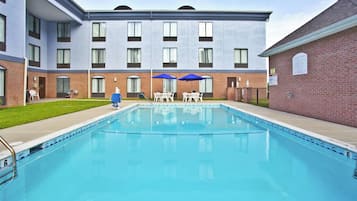 Una piscina con superficie de agua azul cristalina, rodeada por un edificio de ladrillo con varias ventanas y techo plano.