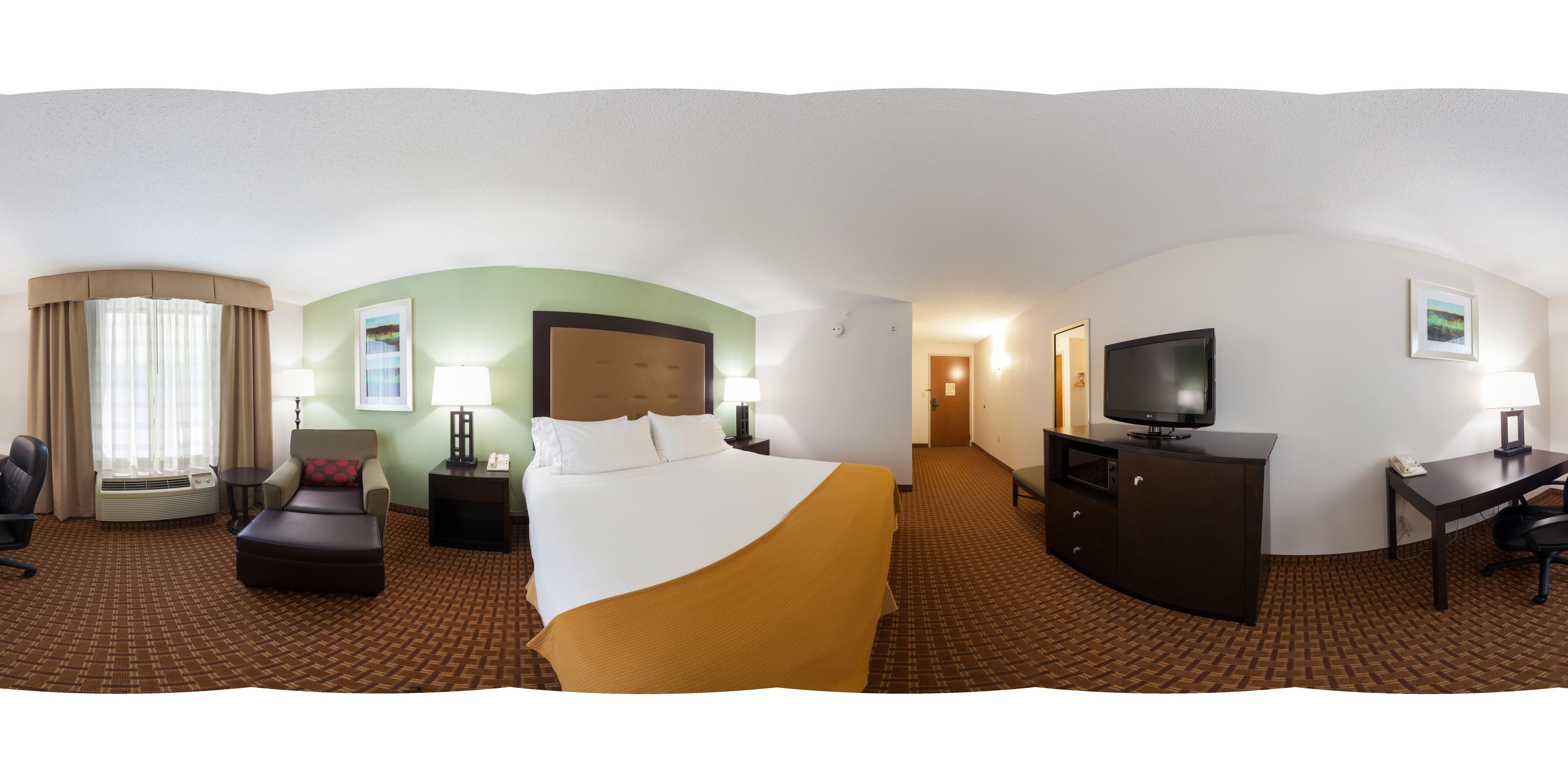 A hotel room with a bed, a desk, a TV, a chair, a lamp, and a window with curtains.