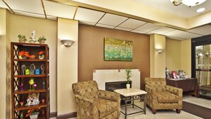 A lobby with two patterned armchairs, a wooden bookshelf with decorative items, and a wall-mounted painting. - Holiday Inn Express Hotel & Suites Harrington-Dover area, DE by IHG (Harrington)