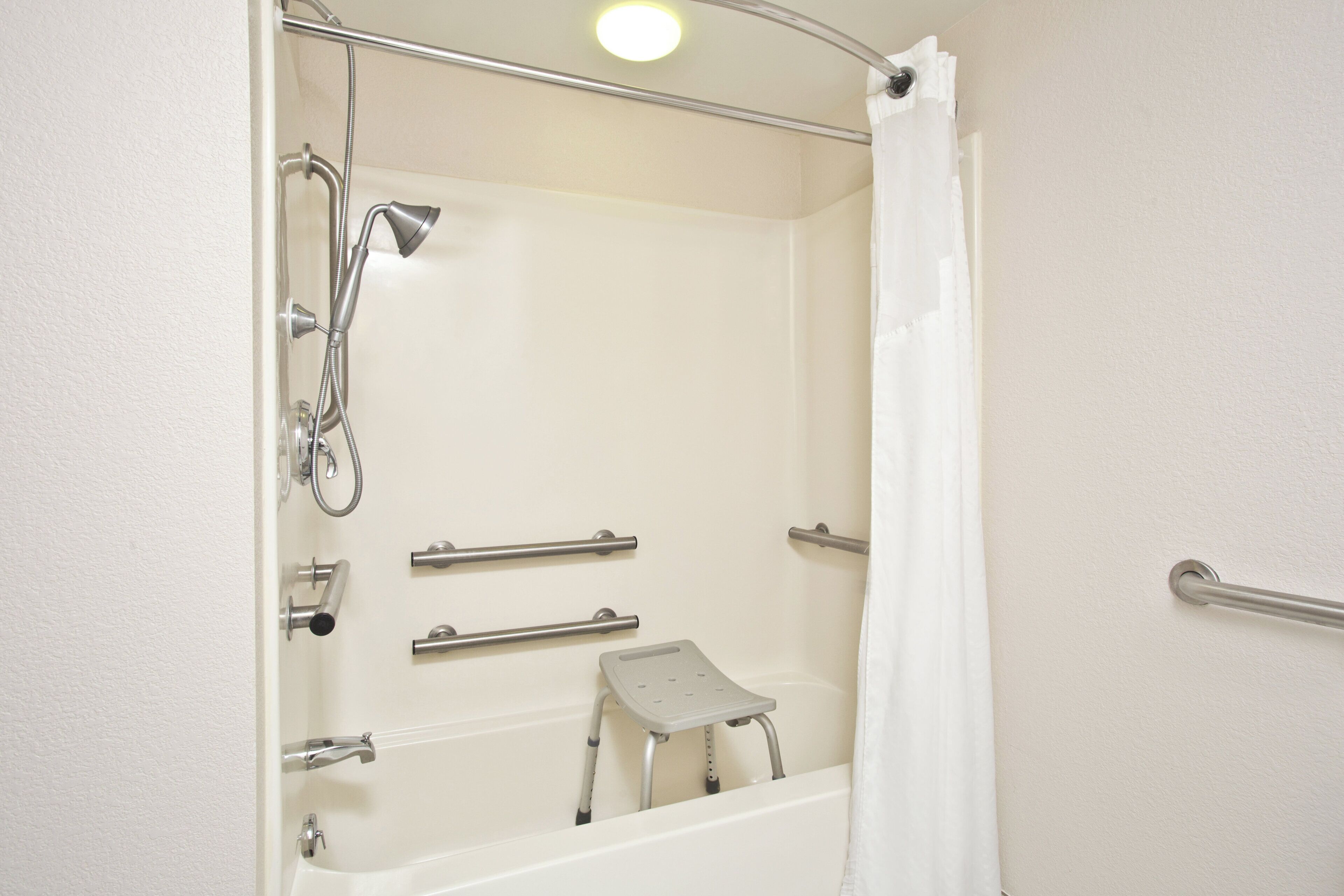 Baño con ducha, barras de apoyo y un taburete.