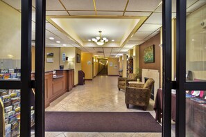 Un hall d'hôtel comprenant un comptoir d'accueil, un guichet d'enregistrement, un espace salon et un couloir menant aux autres chambres.