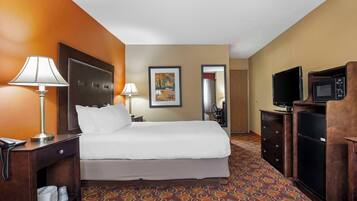Een hotelkamer met een bed, nachtlampjes, een bureau met telefoon, een televisie, een magnetron en een kamerbreed tapijt met een patroon.