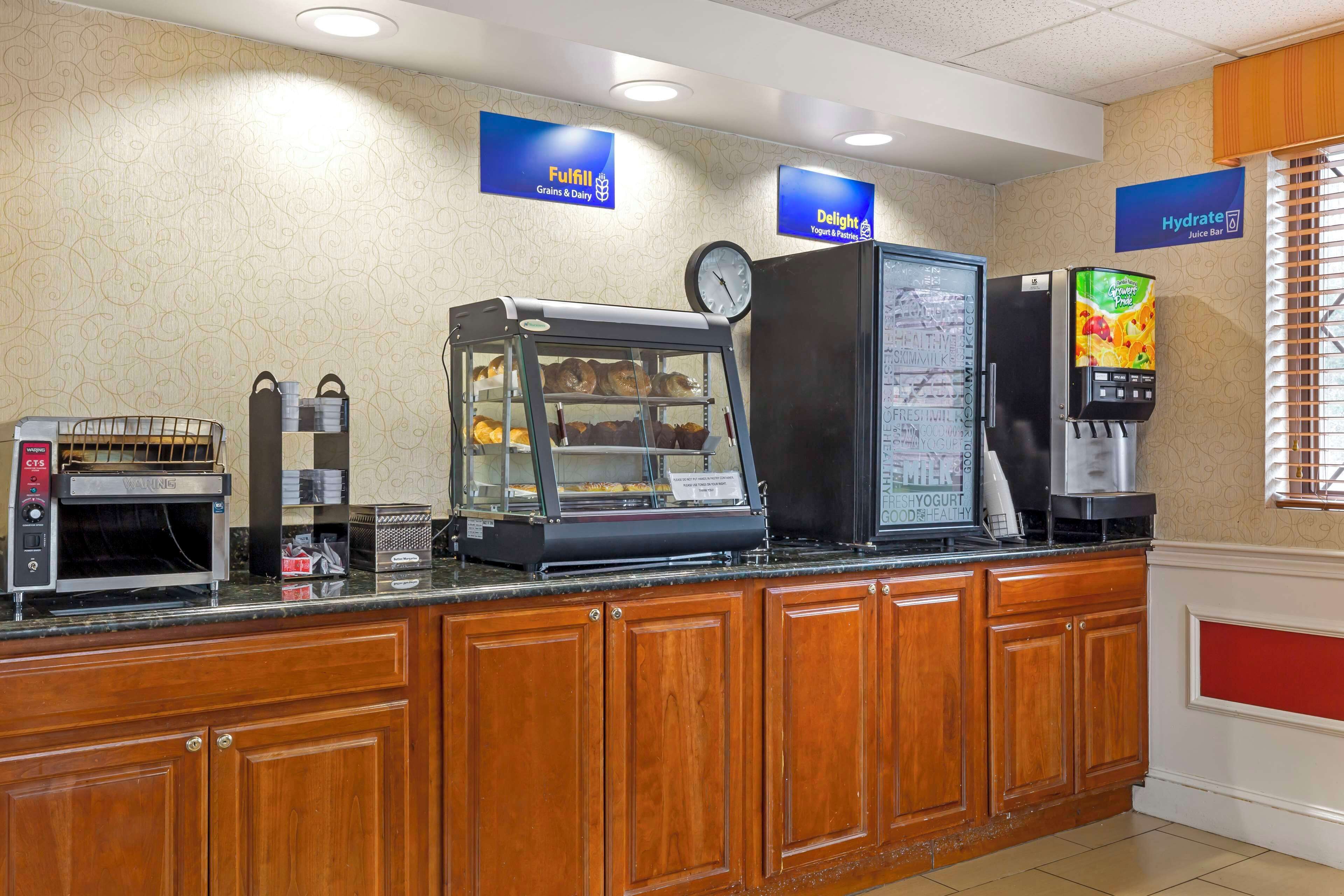 A breakfast bar with a coffee machine, a display case with pastries, a refrigerator, and a juice dispenser.