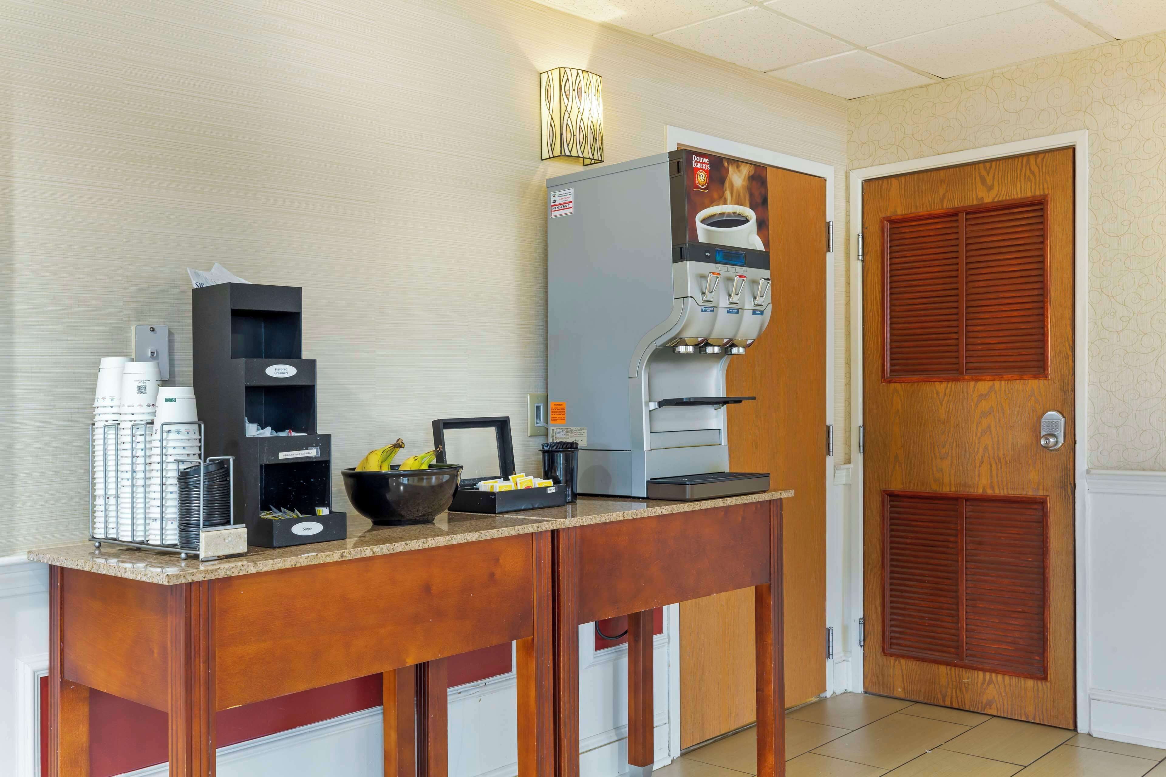 A hotel kitchen with a coffee machine, a bowl of fruit, and a coffee dispenser.