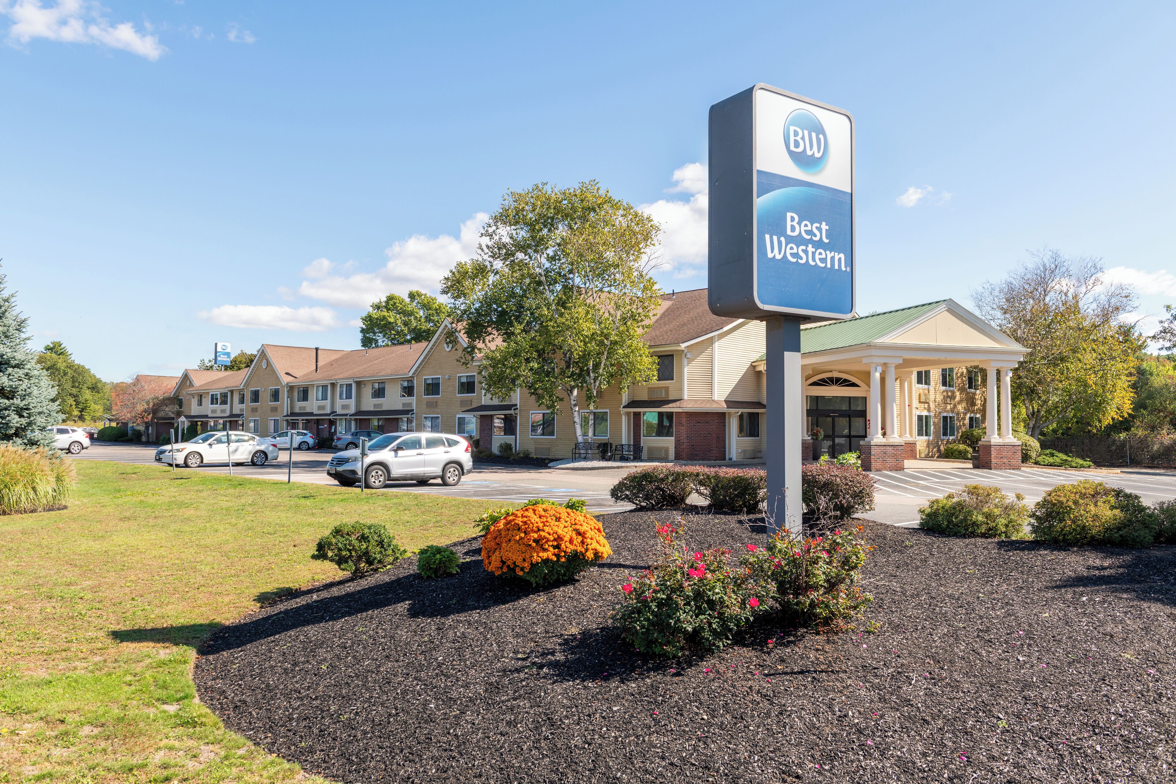 A Best Western hotel with a large sign, a parking lot, and a well-maintained lawn with shrubs and flowers.