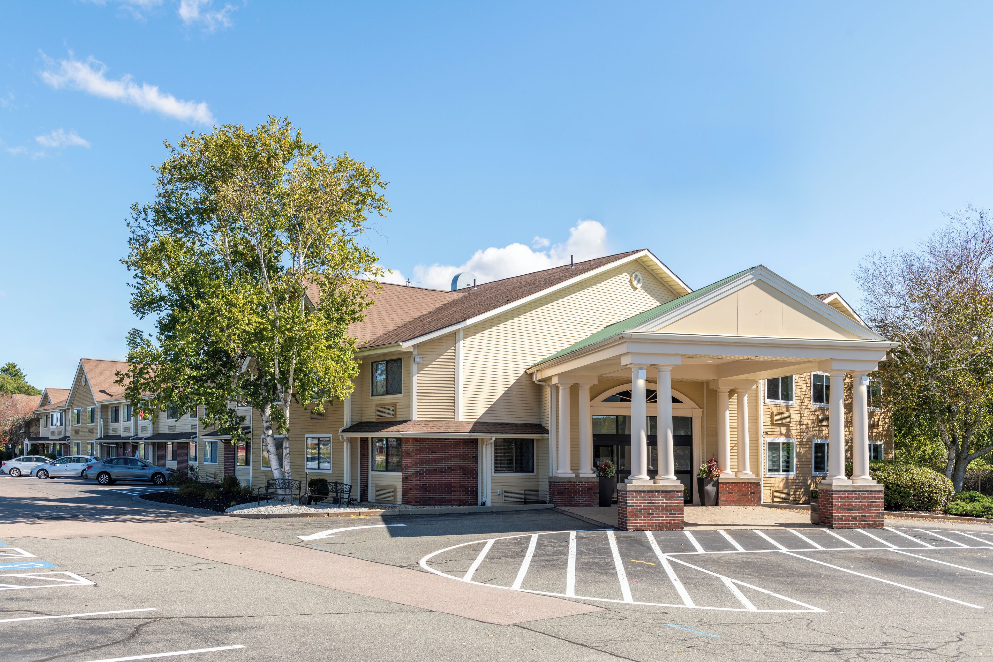 A multi-story hotel with a covered entrance, parking lot, and adjacent buildings.