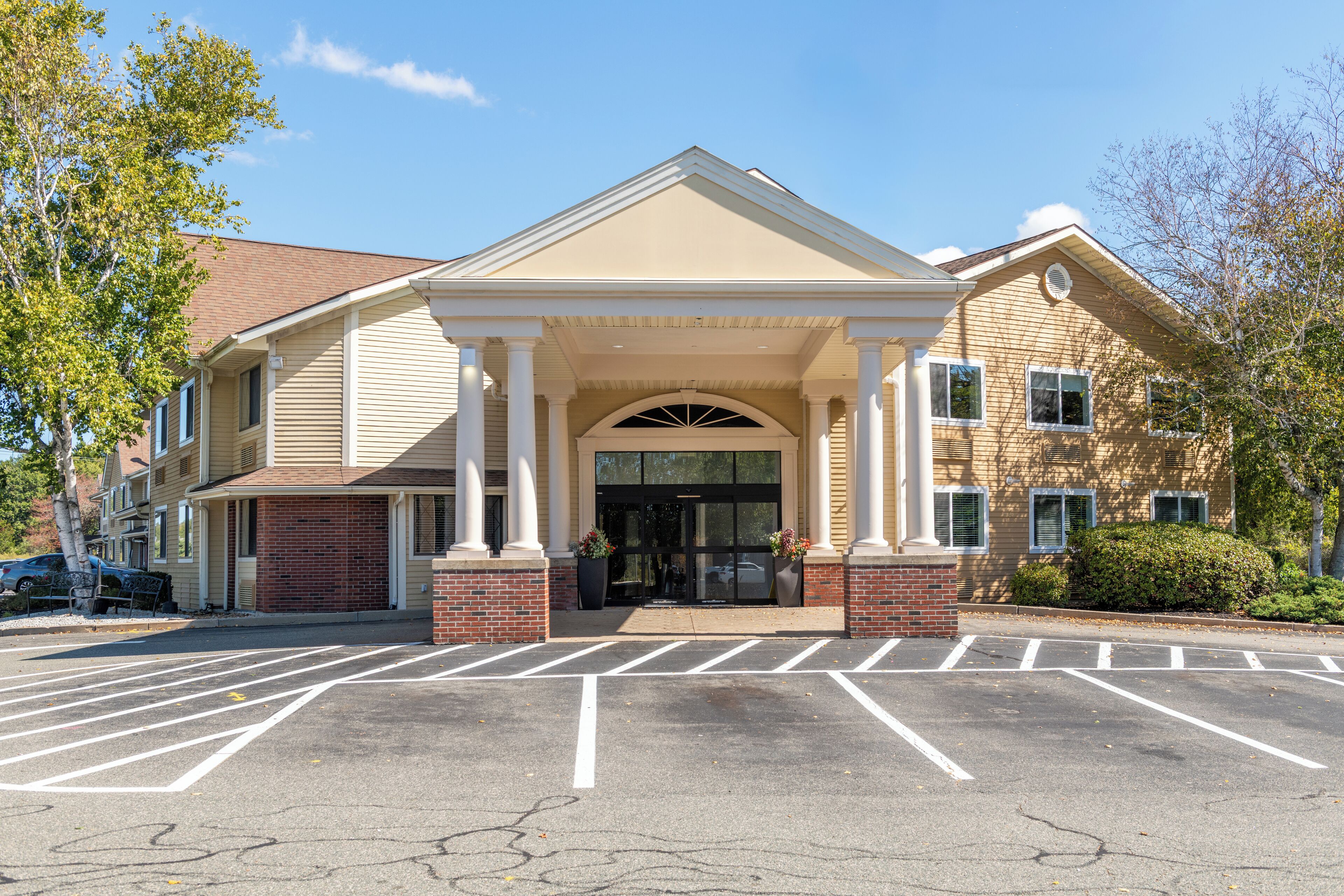 A multi-story building with a central entrance, columns, and a parking lot.