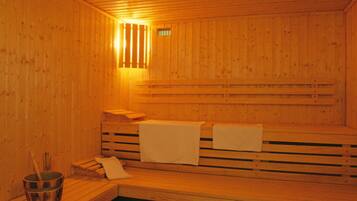 Una sauna de madera con bancos y un asiento de banco, un ventanal pequeño y un cubo con un cepillo.