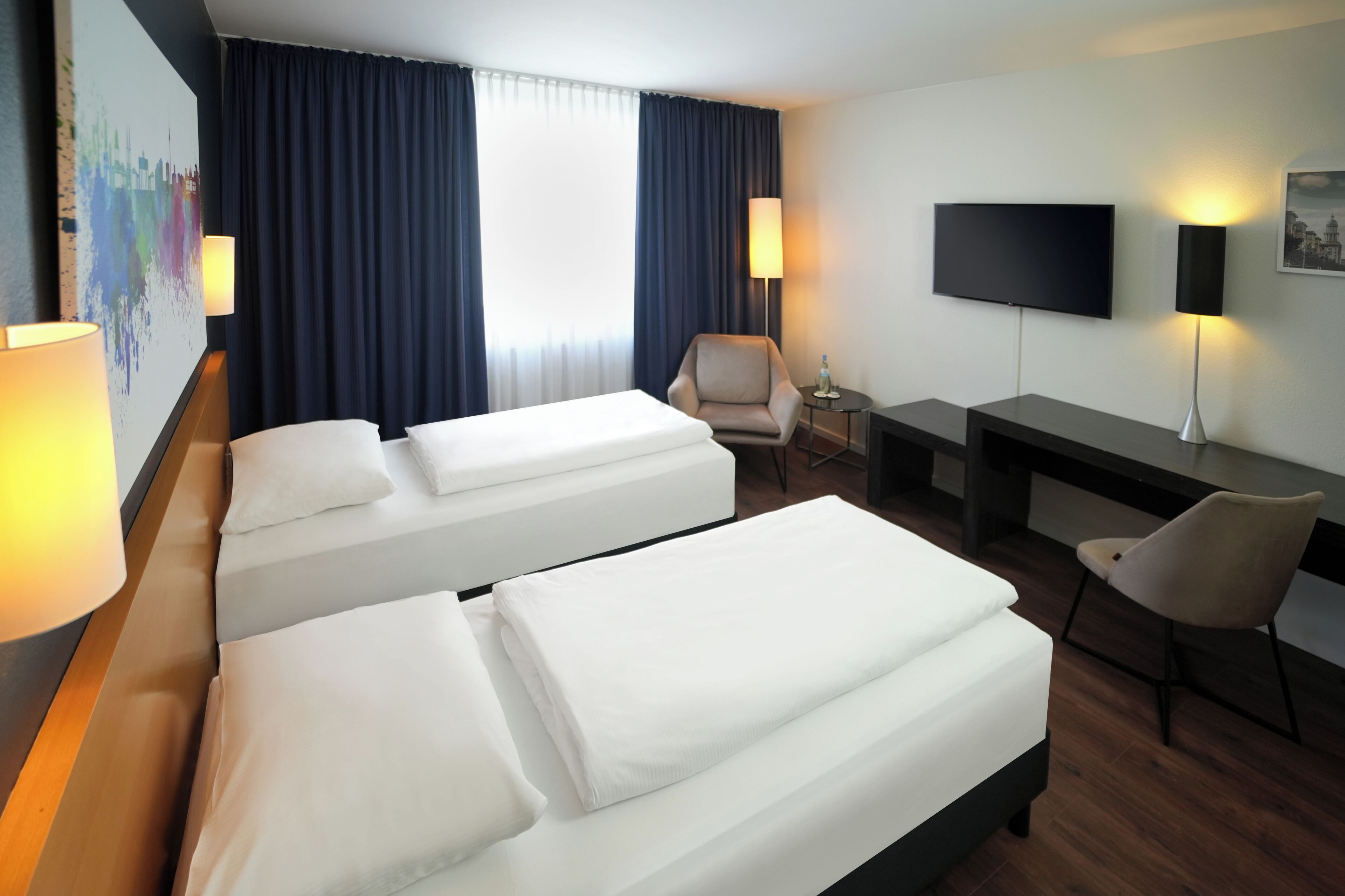 Habitación de hotel con dos camas, un escritorio, una silla, un televisor y una lámpara.