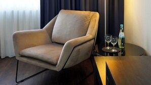 A modern hotel room with a beige armchair, a standing floor lamp, and a small table with two glasses and a bottle. - greet Hotel Potsdam am Park Sanssouci (frisch renoviert) (Potsdam)