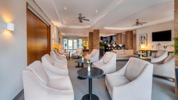 A modern hotel lobby with leather armchairs, a round table with a vase, and a TV mounted on the wall. - greet Hotel Potsdam am Park Sanssouci (frisch renoviert) (Potsdam)