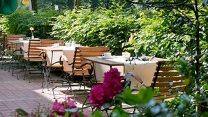 An outdoor dining area with tables and chairs, surrounded by lush greenery and flowers. - greet Hotel Potsdam am Park Sanssouci (frisch renoviert) (Potsdam)