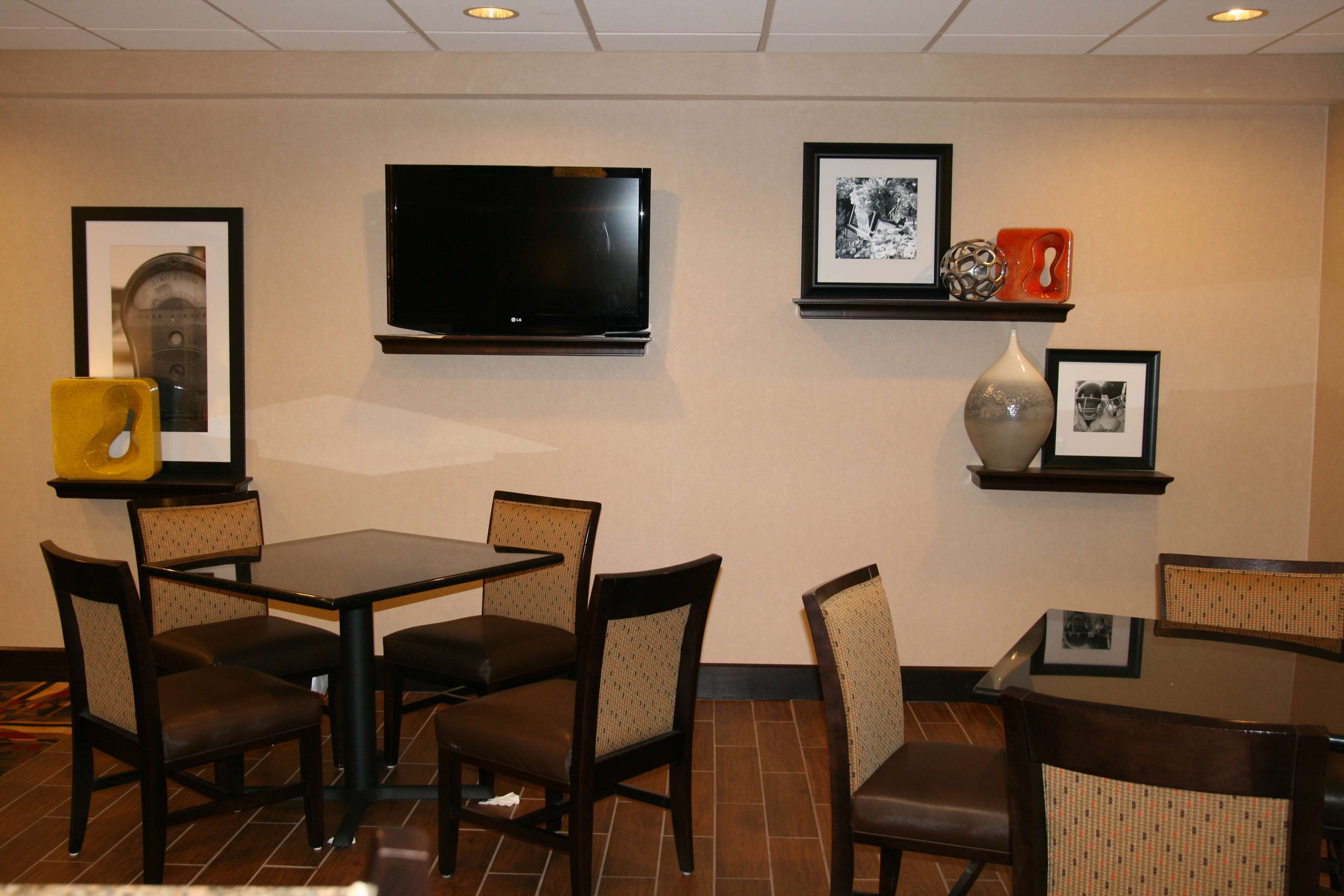 Un espace repas d’hôtel doté d’un téléviseur à écran plat fixé au mur, de tableaux encadrés et d’une petite étagère ornée d’objets décoratifs.