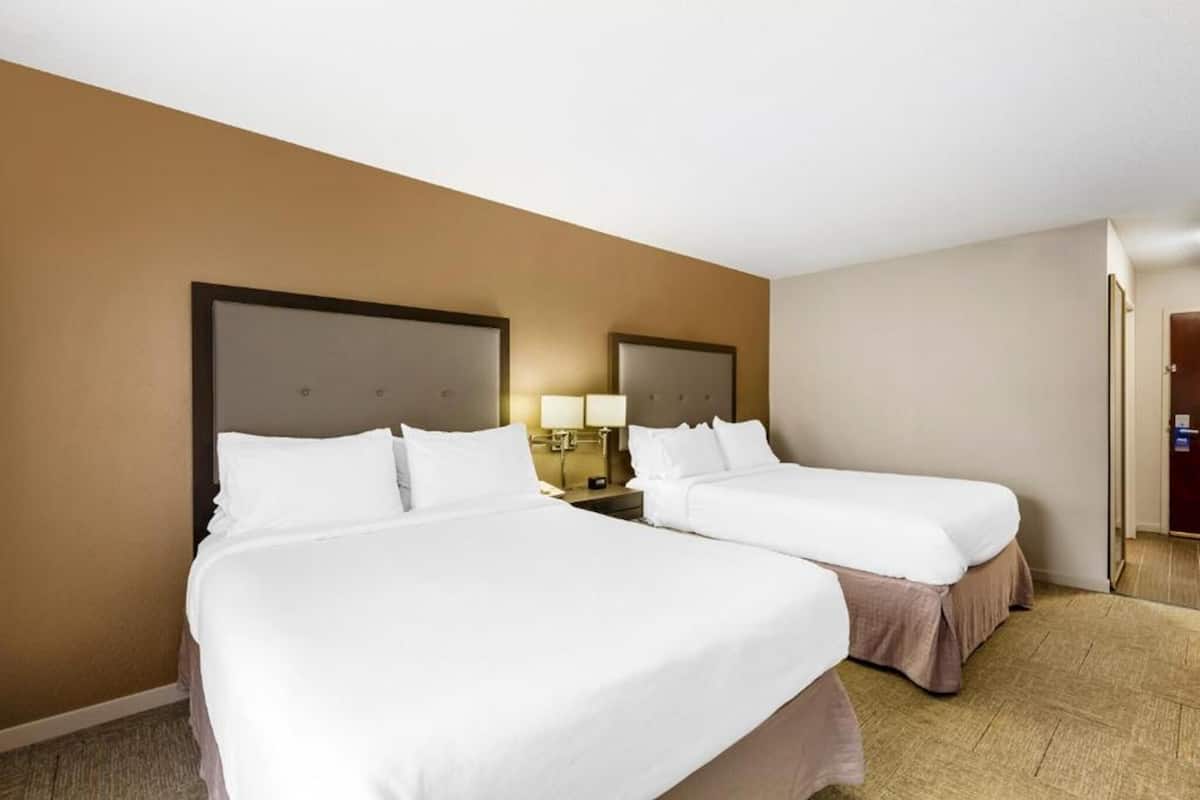 A hotel room with two single beds, a nightstand with a lamp, and a door to the right.