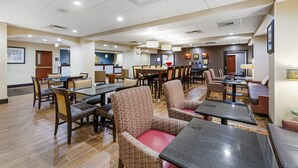 Un hall de hotel con varias zonas de estar, incluyendo mesas y sillas, y un mostrador de recepción.